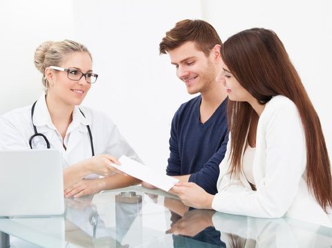 507901839 Female doctor giving prescription paper to couple at desk in clinic
