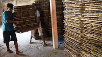 Dua orang pekerja menggotong tumpukan anyaman bambu yang berisi kerupuk untuk dijemur.