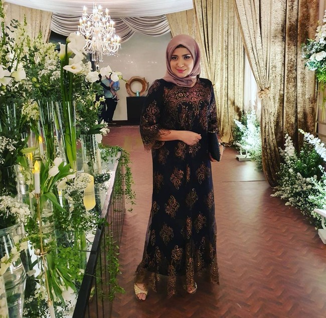 Ketika menghadiri acara pernikahan, Rahma Sarita memakai dres motif warna hitam dan hijab dengan warna senada. Wanita 45 tahun itu mengikat rapi hijabnya ke belakang dan hanya menggunakan satu jarum pentul yang berada di bawah lehernya. Foto: Instagram @rahmasarita_jufri