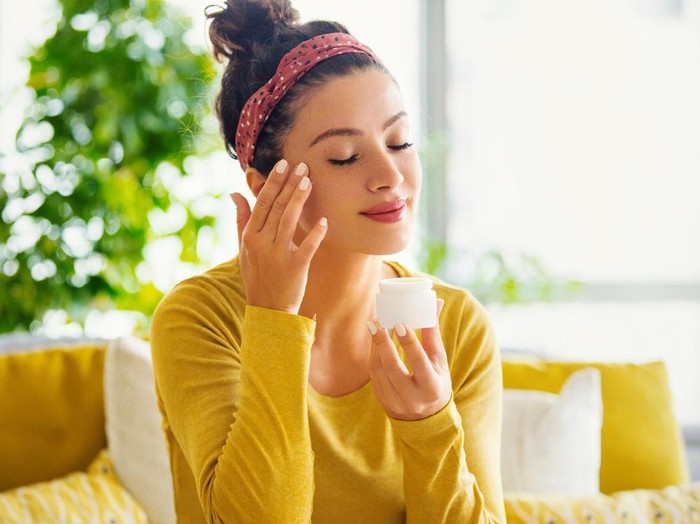 Young woman with eyes closed applying face cream.