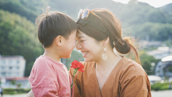 Asian boy presenting his mother a red carnation flower for Mothers Day.