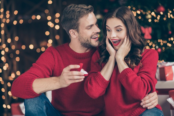 Kado Natal Perhiasan Photo of couple in decorated garland lights room guy giving lady unexpected, engage ring box waiting answer sitting cozy near x-mas tree indoors wear red sweaters