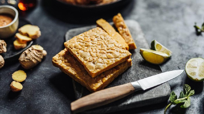 Tempe Close-up of tempeh on cutting board with kitchen knife with other ingredients on table. Preparing a vegan dish in kitchen.