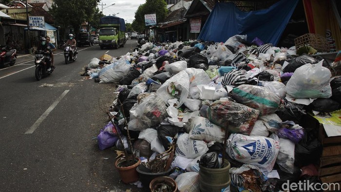 Warga melintas di depan tumpukan sampah yang membludak menutupi separuh jalan di depan gerbang Kampung Bausasran, Kota Yogyakarta, Senin (21/12/2020).