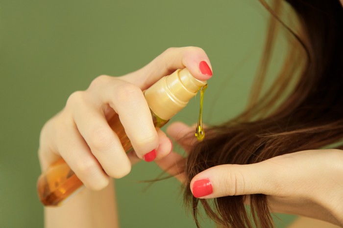 1175291168 Woman applying oil on hair ends, split hair tips, dry hair or sun protection concept