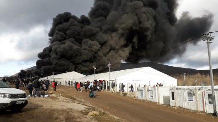 Refugees leave a camp as a fire burns, near the northwestern village of Lipa, Bihac region, on December 23, 2020. - A refugee camp in Bosnia criticised for its bleak conditions was destroyed in a fire on December 23 police said, as the country faces a repeat crisis over where to shelter migrants during winter. There were no casualties or injuries, but the infrastructure of the site near the northwestern village of Lipa was destroyed, police spokesperson Ale Siljdedic told AFP. (Photo by STR / AFP)
