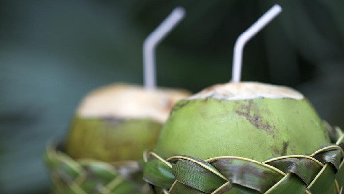 Fresh Brazilian coco gelado drinking coconuts in woven palm baskets rest on weathered wooden table against green jungle background
