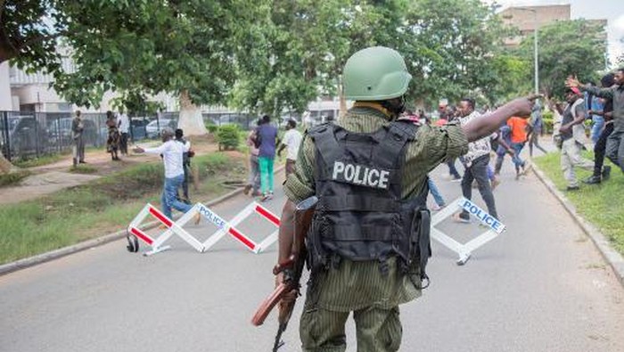 A police officer gestures towards supporters of opposition United Party for National Development (UPND) leader Hakainde Hichilema as he was being questioned at the Lusaka Police Force headquarters in Lusaka, Zambia, on December 23, 2020. - Two demonstrators were killed on December 23, 2020 in a protest outside the police headquarters in the Zambian capital Lusaka, where opposition leader Hakainde Hichilema was being questioned. (Photo by SALIM DAWOOD / AFP)