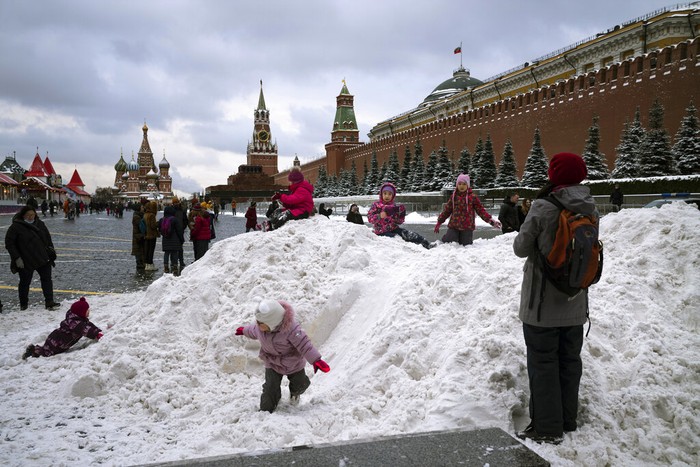 A boy plays on a pile of snow in Red Square decorated for Christmas and New Year celebrations, without the Christmas Market due to the virus-related restrictions, with the Kremlin Wall, the Historical Museum and GUM in the background in Moscow, Russia, Saturday, Dec. 26, 2020. The temperature in Moscow is about 0 degree Celsius (32 degree Fahrenheit). (AP Photo/Alexander Zemlianichenko)