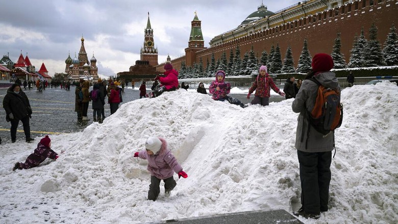 A boy plays on a pile of snow in Red Square decorated for Christmas and New Year celebrations, without the Christmas Market due to the virus-related restrictions, with the Kremlin Wall, the Historical Museum and GUM in the background in Moscow, Russia, Saturday, Dec. 26, 2020. The temperature in Moscow is about 0 degree Celsius (32 degree Fahrenheit). (AP Photo/Alexander Zemlianichenko)