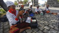 Tiba di spot ikonik bertuliskan TANAH LOT, sekumpulan fotografer dengan baju seragam berwarna putih duduk santai.