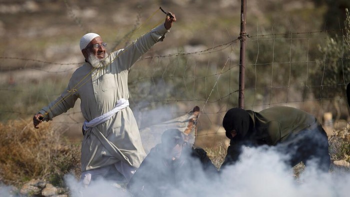 Palestinian protesters use slingshots to hurl stones towards Israeli troops during a protest against Israeli settlements, in the West Bank village of Deir Jarir, north of Ramallah, Friday, Jan. 1, 2021. (AP Photo/Majdi Mohammed)