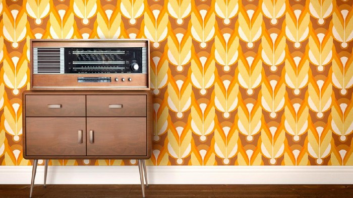 Vintage old radio from eastern Europe (labels indicate cities of the eastern block, including former GDR, East Germany) laying on a piece of furniture and a background showing a sixties, seventies design wallpaper pattern. Copy space on the side for customization.