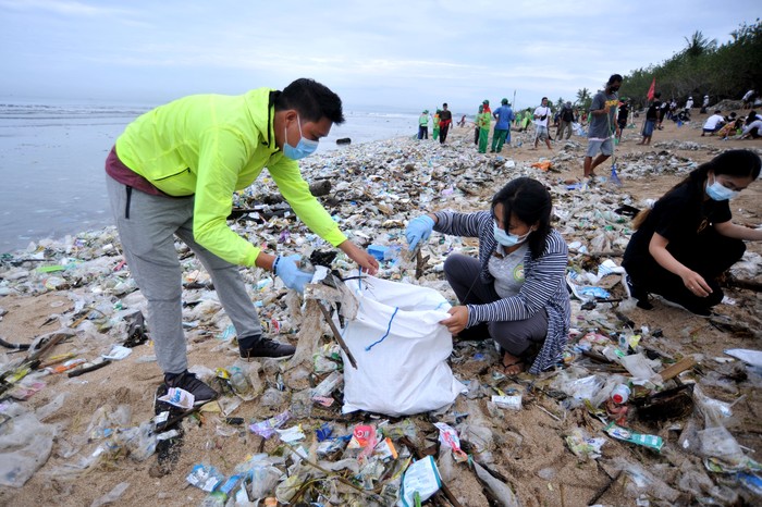 Relawan membersihkan sampah yang berserakan saat mengikuti aksi bersih sampah di Pantai Kuta, Badung, Bali, Rabu (6/1/2021). Kegiatan yang diikuti ratusan orang dari berbagai unsur masyarakat tersebut dilakukan untuk membersihkan sampah kiriman yang terbawa arus gelombang laut dan terdampar kawasan Pantai Kuta yang mengganggu aktivitas warga serta wisatawan. ANTARA FOTO/Fikri Yusuf/aww.