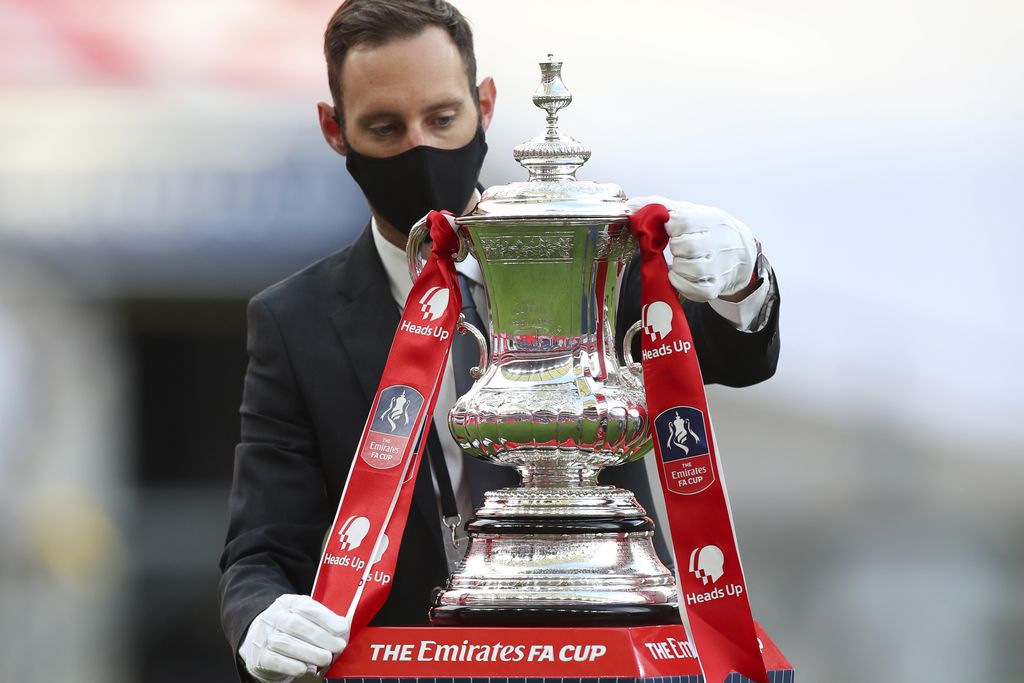 The trophy is handled by a man wearing a face mask after the FA Cup final soccer match between Arsenal and Chelsea at Wembley stadium in London, England, Saturday, Aug.1, 2020. (Catherine Ivill/Pool via AP)