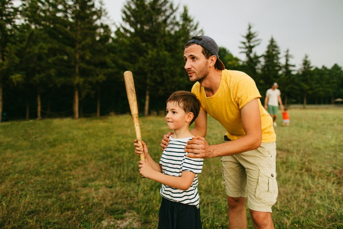 Young father sharing basics of baseball with his little boy, outdoors in the park