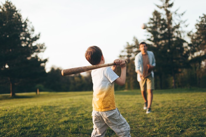Young father sharing basics of baseball with his little boy, outdoors in the park