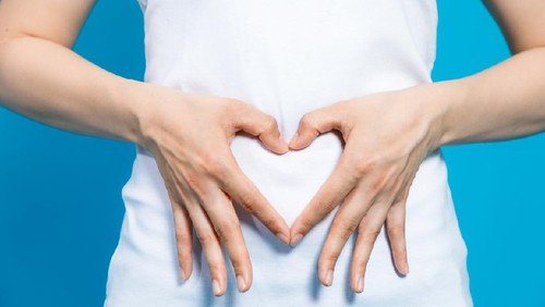 young woman who makes a heart shape by hands on her stomach.
