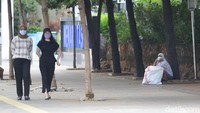 Dua orang warga berjalan diantara seorang tunawisma yang sedang duduk.