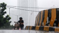 Pengendara mendorong sepeda motornya yang mogoh di bawah guyuran hujan.
