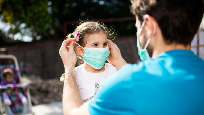 Single father applying pollution mask to his daughter. They are outside.