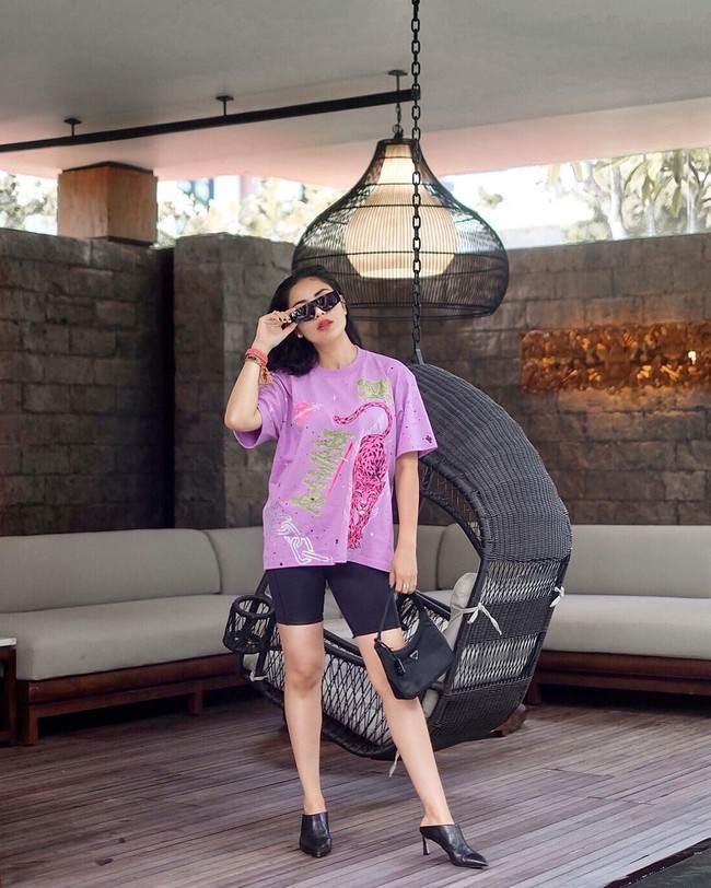 Berpose di Apurva Kempinski Bali, Nindy memadukan gaya santai dengan kaus oversized, celana spandeks dan mules boots. Ia juga tampak menjinjing tas Prada. Foto: Instagram/@mozawahyu, @nindyparasadyharsono