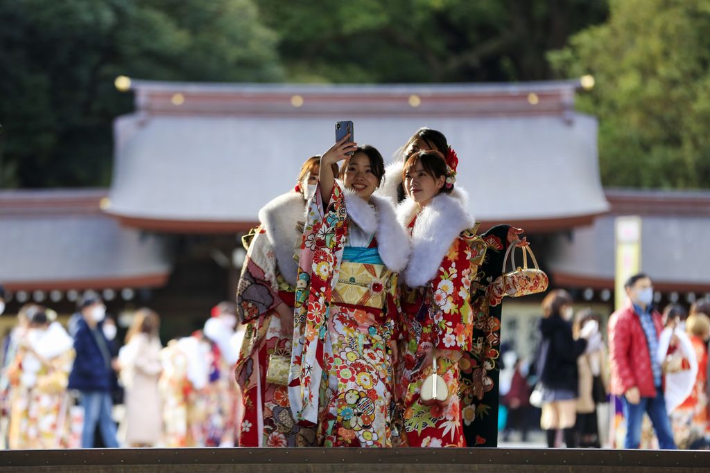 Kimono-clad women wearing face masks to protect against the spread of the coronavirus pose for a selfie while visiting a Shinto Shrine as they celebrate Coming-of-Age, turning 20 years old, the traditional age of adulthood in Japan, Monday, Jan. 11, 2021, in Tokyo. Most of the city hosted ceremonies were cancelled due to a state of emergency. (AP Photo/Kiichiro Sato)