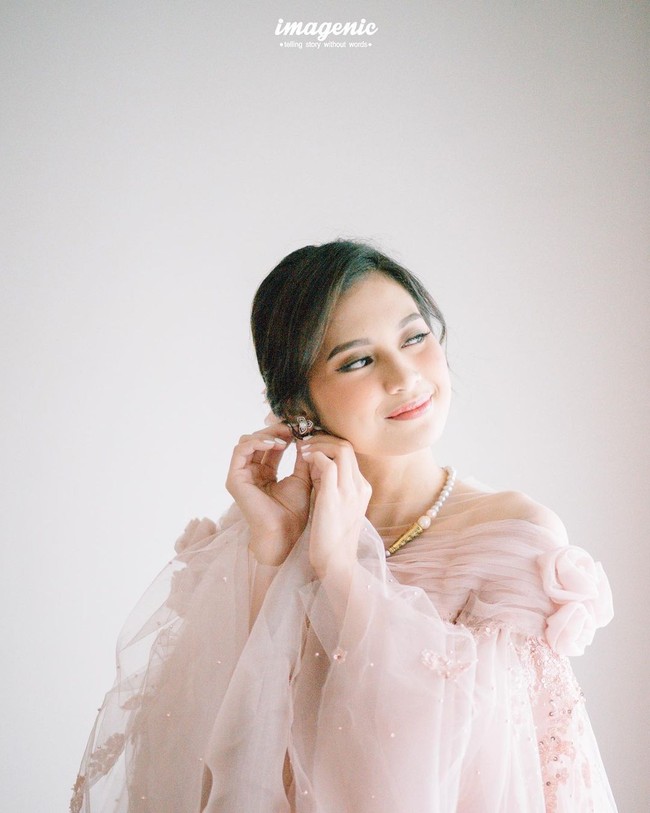 Tampil anggun dengan tata rambut sanggul, ia pun menambahkan aksesori kalung mutiara yang memberi sentuhan klasik dan tradisional pada penampilan. Sedangkan untuk makeup, wanita 23 tahun tersebut terlihat menerapkan sapuan warna pink lembut yang serasi dengan busana. Foto: Instagram @imagenic