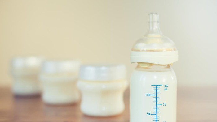Baby bottle with milk and a measuring scale on the background of a lot of full bottles of breast milk. Mothers milk - the most healthy food for newborn