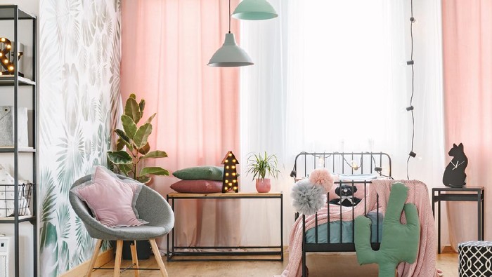 Pink pillow on grey armchair near bed in girls bedroom interior with green cactus and lights on table