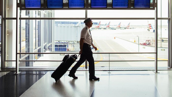 1054932270 Chicago, IL, USA - July 17, 2017: Pilot walking through OHare Airport terminal with the arrivals and departures board in background.