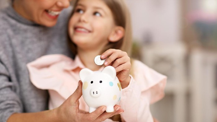 Picture of young girl and her mother with piggybank sitting at table