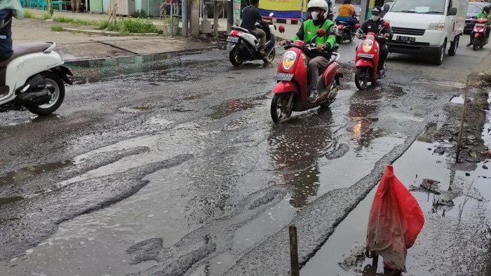 Jalan Caman Raya rusak berlubang hingga digenangi air selokan.