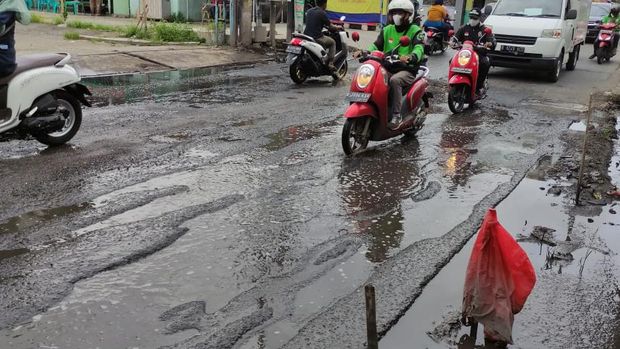 Jalan Caman Raya rusak berlubang hingga digenangi air selokan.