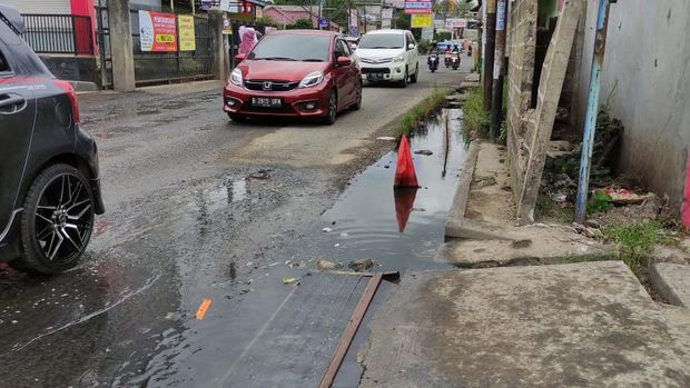 Jalan Caman Raya rusak berlubang hingga digenangi air selokan.