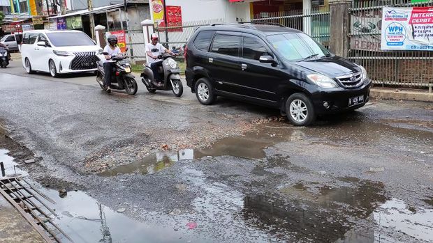 Jalan Caman Raya rusak berlubang hingga digenangi air selokan.
