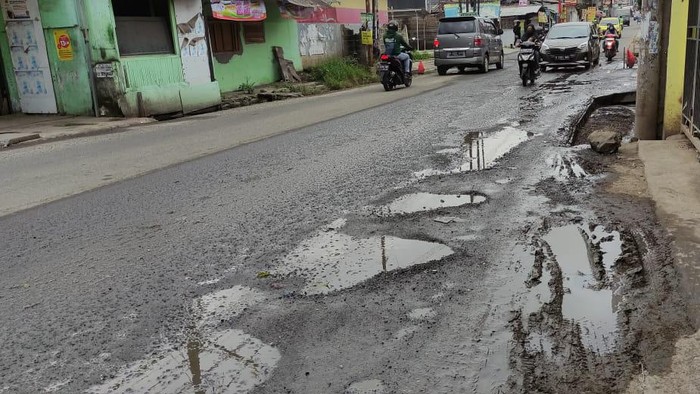 Jalan Caman Raya rusak berlubang hingga digenangi air selokan.