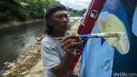 Para seniman terus menggoreskan kuas untuk menyelesaikan pembuatan mural di bantaran Sungai Ciliwung.
