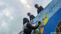 Beberapa anak melongok dari atas dinding turap untuk melihat proses pembuatan mural.