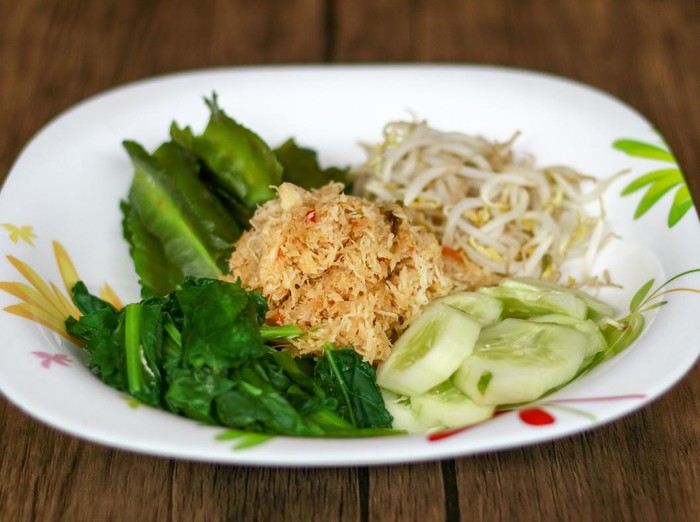 Urap Sayur urap on wood background. Cooked vegetables with spiced grated coconut. Indonesian traditional food.