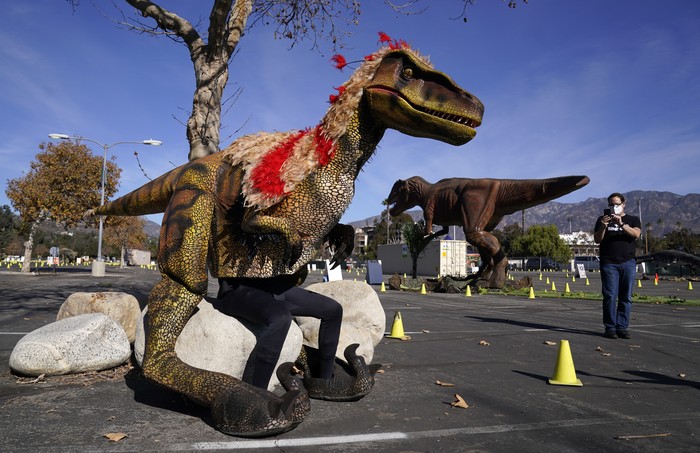 Jose Correa, left, takes a rest before working a raptor model at the Jurassic Quest Drive-Thru Experience on Friday, Jan. 15, 2021, at the Rose Bowl in Pasadena, Calif. The touring exhibit features over 70 moving and life-like dinosaurs, and runs through January 31. (AP Photo/Chris Pizzello)