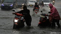 Pengendara terpaksa mendorong motornya yang mogok akibat menerobos banjir.