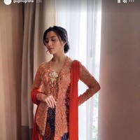 Sedangkan bawahannnya, dipilih batik dengan campuran warna oranye dan biru tua yang menyatu dengan keseluruhan gaya. Sedangkan untuk sepatu, calon mempelai itu memakai high heels dengan detail embellishment yang juga bernuansa peach. Foto: Instagram @guginugraha