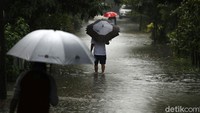 Sejumlah warga melintas di jalanan yang terendam banjir.