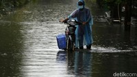 Pengendara mendorong motornya yang mogok akibat menerobos banjir.