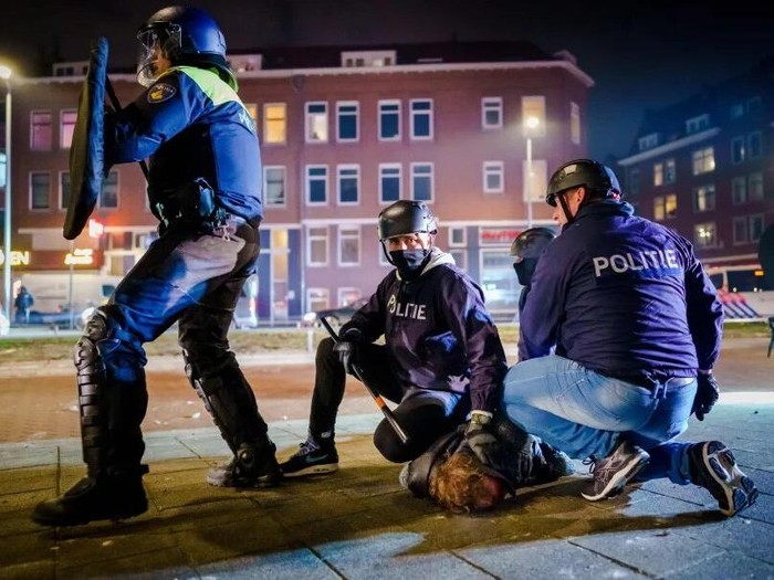 Dutch policemen arrest a man during clashes with a large group of young people on Beijerlandselaan in Rotterdam, on January 25, 2021. - The Netherlands was hit by a second wave of riots on January 25 evening after protesters again went on the rampage in several cities following the introduction of a coronavirus curfew over the weekend. Riot police clashed with groups of protesters in the port city of Rotterdam, where they used a water canon. (Photo by Marco de Swart / ANP / AFP)