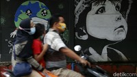 Warga melintas di depan mural bertema COVID-19, di jalan Raya Bukit Duri, Manggarai, Jakarta, Rabu (27/01/2021).