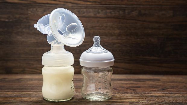 Baby bottle with breast pump attachement and empty bottle against a wood background