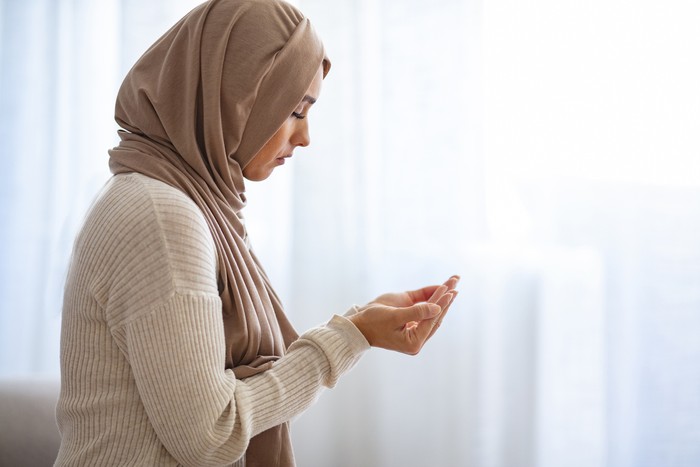 Ilustrasi wanita muslim Young Woman Praying. Young Muslim woman praying, indoors. Young Muslim woman in beige hijab and traditional clothes praying for Allah, copy space. Arab Muslim woman praying