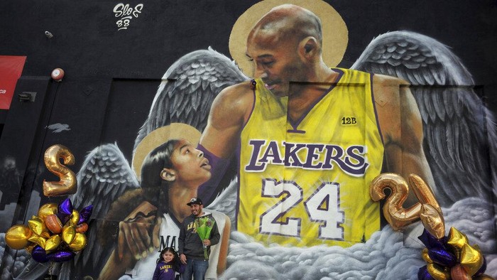 Jose Jara with his three-year-old daughter Giana poses for a picture in front of a mural on the side of Hardcore Fitness along Pico Blvd as fans of Kobe Bryant celebrate the life and legacy around murals and makeshift memorials in Los Angeles on Tuesday, Jan. 26, 2021. (Keith Birmingham/The Orange County Register via AP)